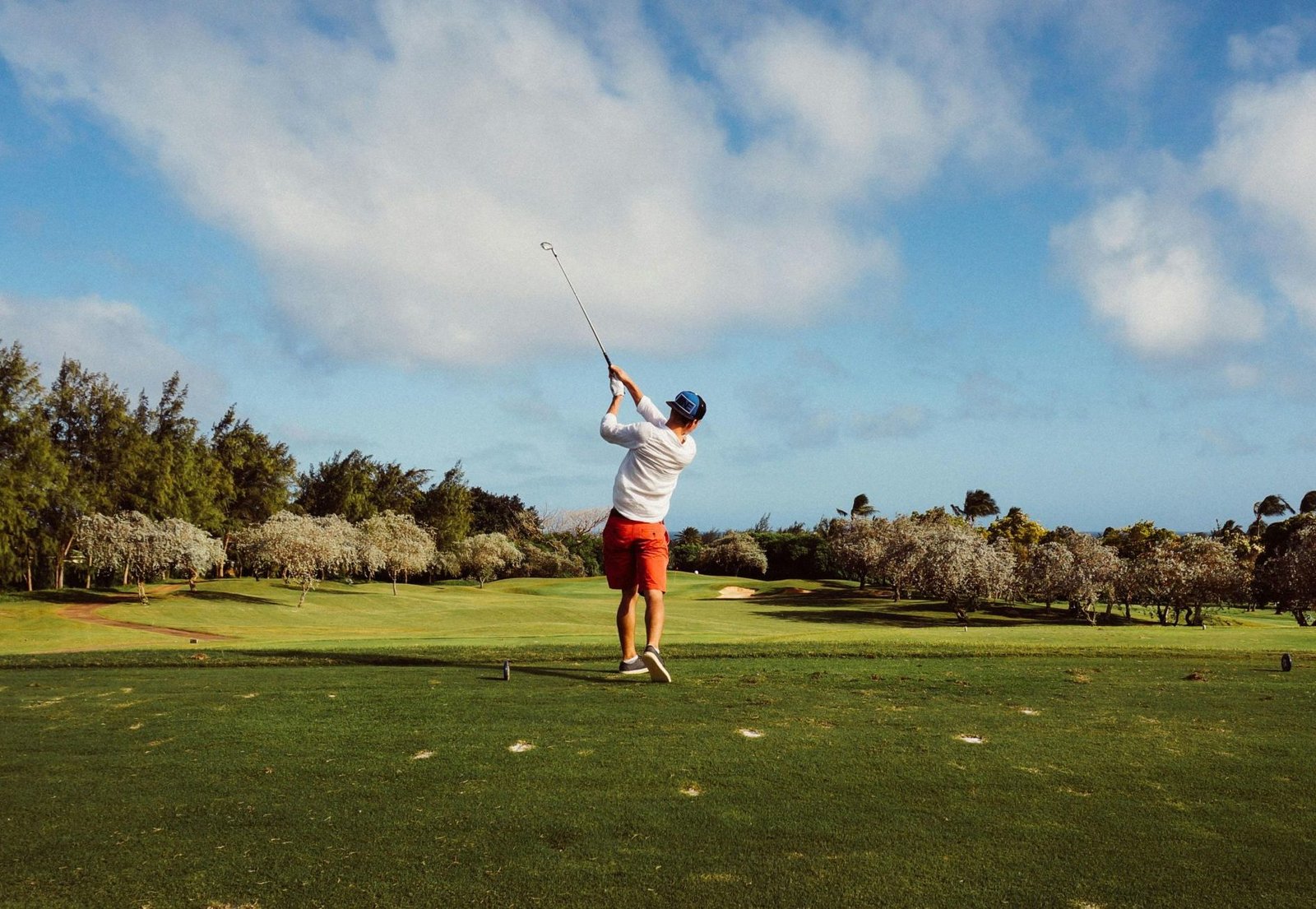 A golfer swings on a picturesque golf course with lush greenery and a clear blue sky, epitomizing outdoor leisure.